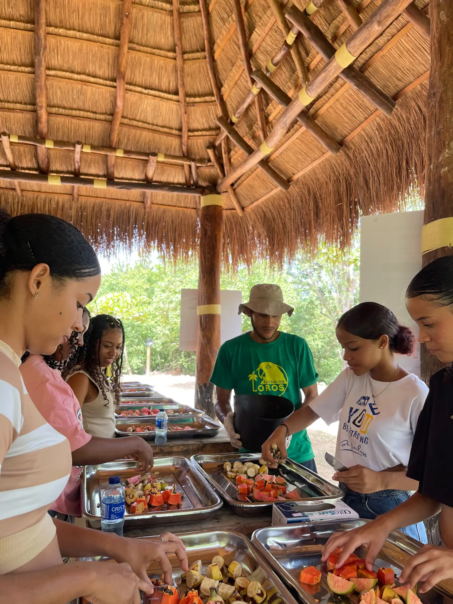 Jóvenes preparando la fruta para los loros y guacamayas junto al equipo de la fundación, bajo una enramada en la reserva